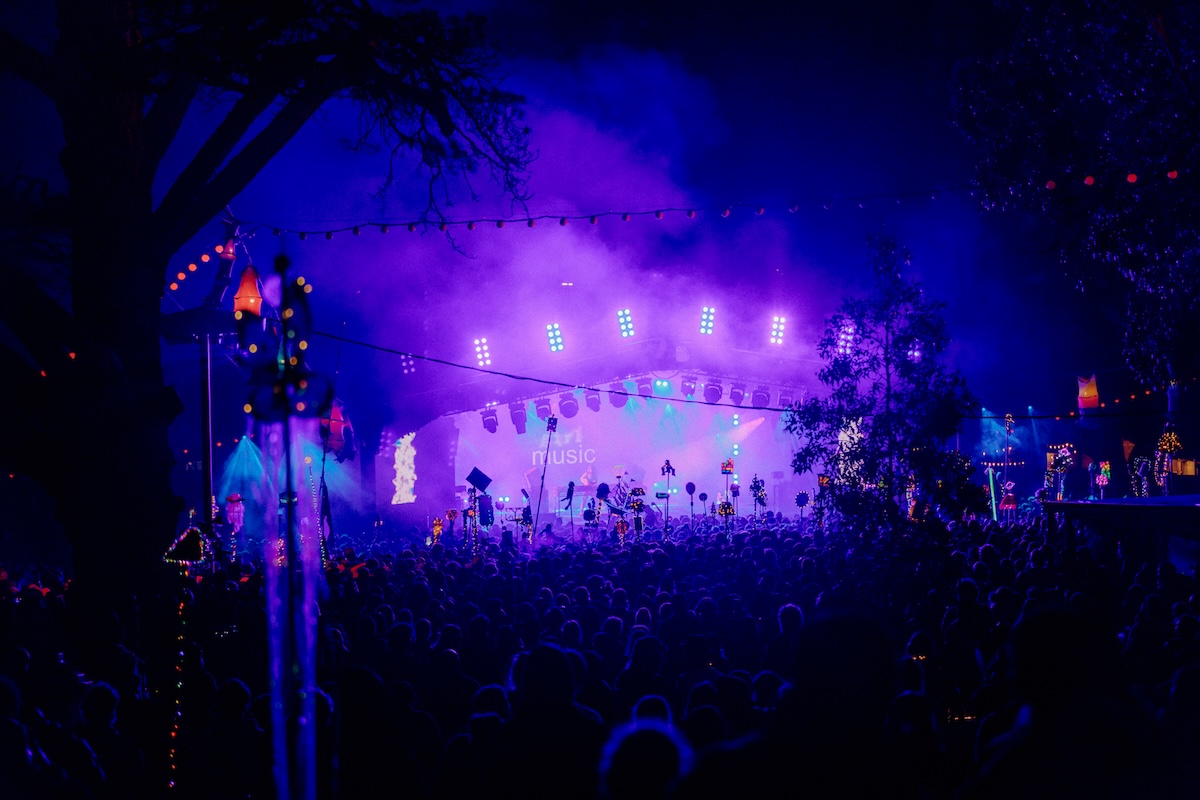Golden Plains Festival stage illuminated at night by bright purple and blue lights with a large crowd gathered in front of the illuminated trees.